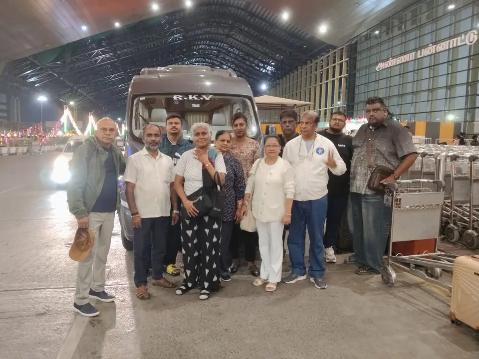 Group of travellers with luggage trolleys beside an RKV tempo traveller at the airport at night