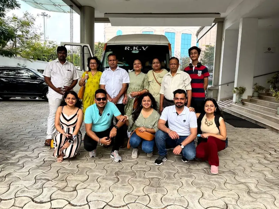 Corporate team posing at a hotel entrance before boarding their RKV tempo traveller