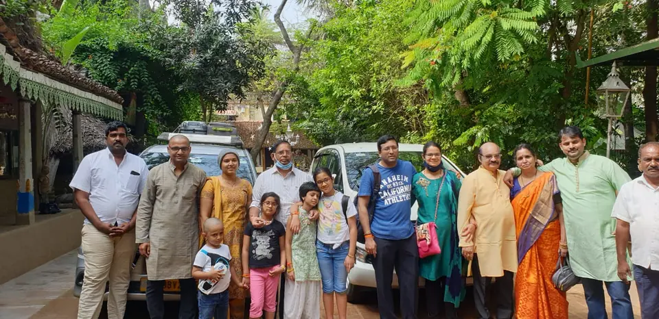Extended family group in traditional wear standing in a garden with their vehicle