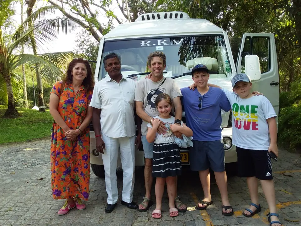 Family with children posing with our driver in front of a tempo traveller under coconut trees
