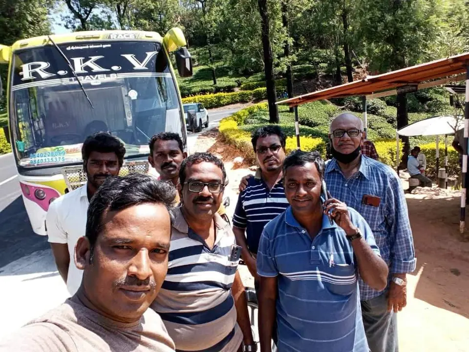 Selfie of a men's tour group beside an RKV coach at a hill-station garden