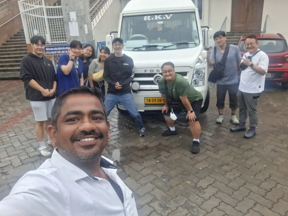 Selfie of our driver with an East Asian tour group beside an RKV tempo traveller