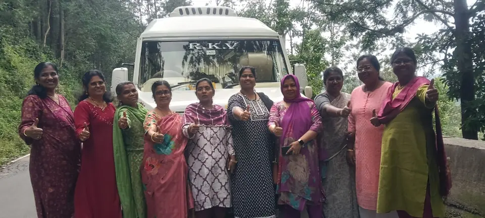 Ladies group in sarees standing in front of a tempo traveller on a pilgrimage trip