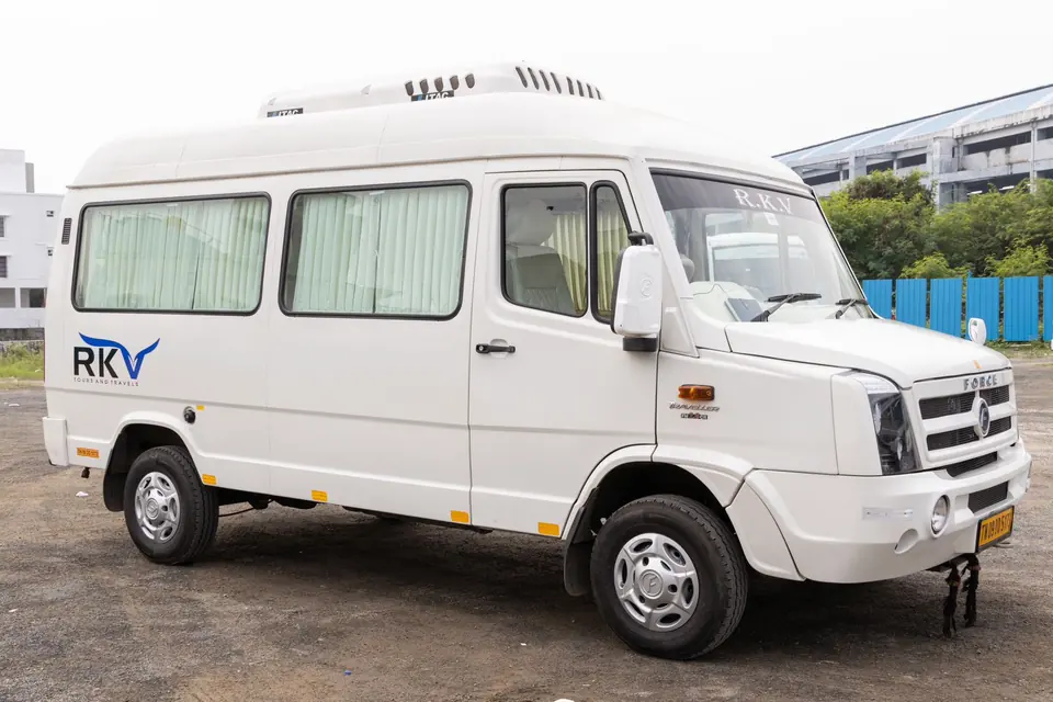 Long-body white tempo traveller with large side windows parked outside a Chennai building