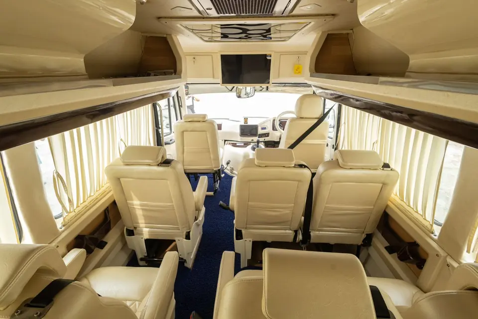 Maharaja tempo traveller cabin seen from the rear, with cream sofa seats, curtains and a TV