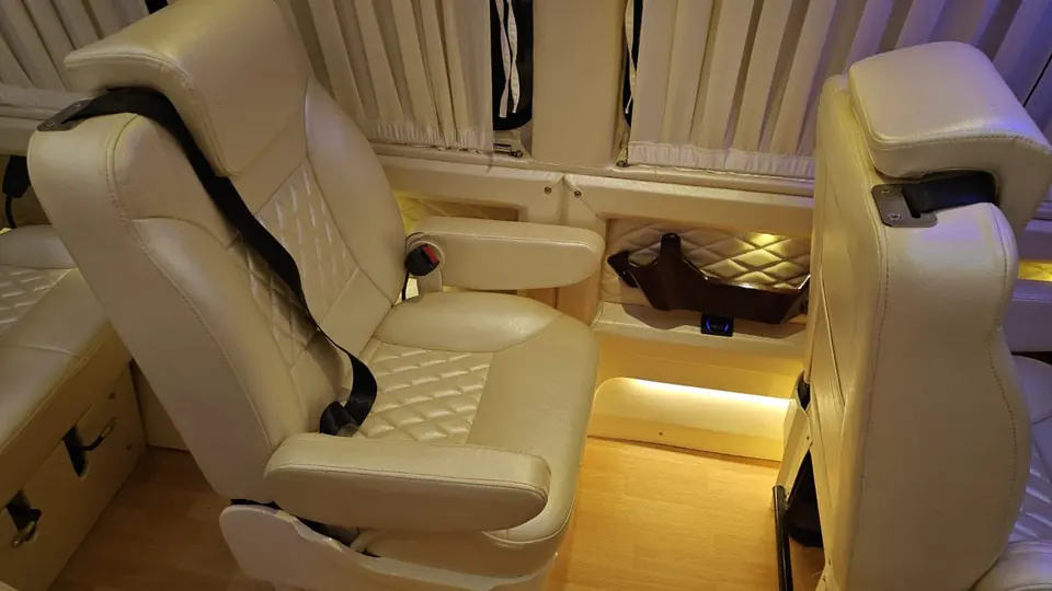 Close view of a cream recliner seat with warm floor lighting in a Maharaja tempo traveller