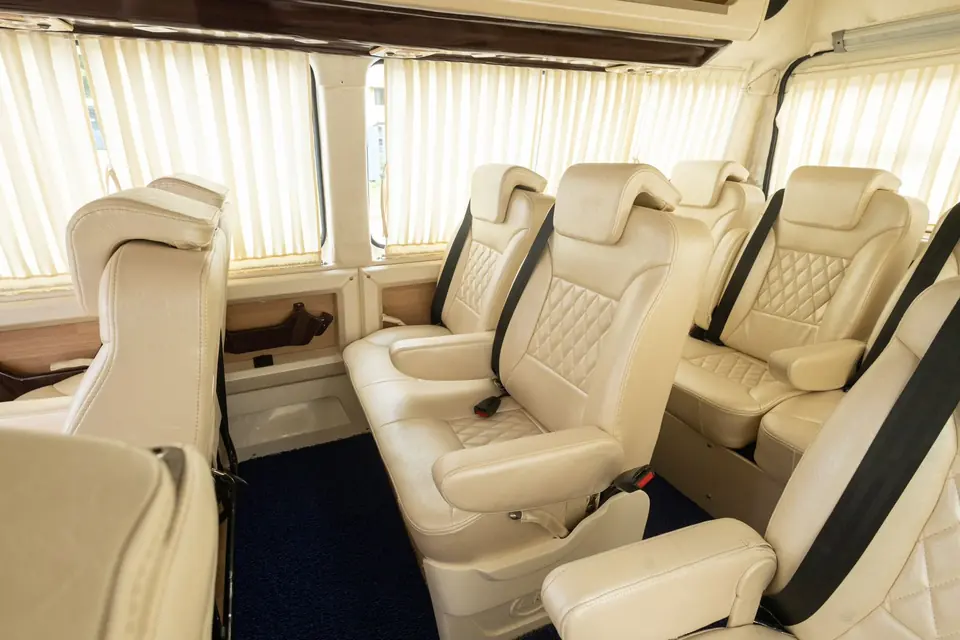 Side view of cream leather sofa-style recliner seats with seat belts in a Maharaja tempo traveller