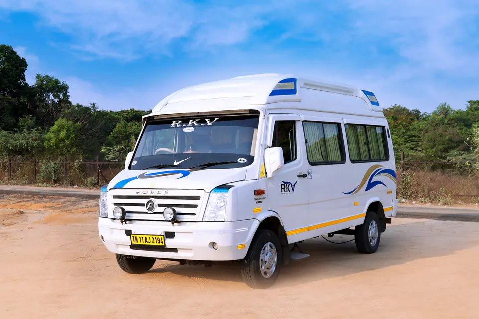 RKV tempo traveller parked on open ground, front angle showing grille and roof AC unit