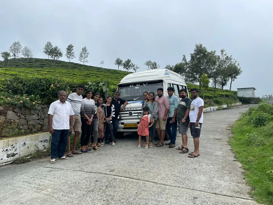 Family group beside an RKV tempo traveller on a road through a tea estate in the hills